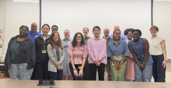 A photo of members of the Center for Disability Justice Advisory Board. Everyone is standing at the front of a classroom smiling at the camera. There are 15 people in the photo.