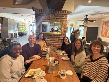 Six smiling people sitting around a wooden table in a restaurant.