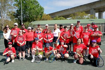 A group of people in red tshirts on tennis court representing the Special Olympics organization